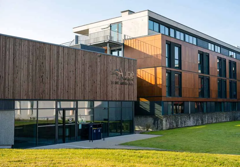 Le bâtiment du Centre sportif de l’Aube, façade en bois et verre sur une pelouse