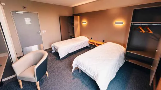 Une chambre confort du Centre sportif de l’Aube : deux lits simples, un fauteuil, une penderie ouverte
