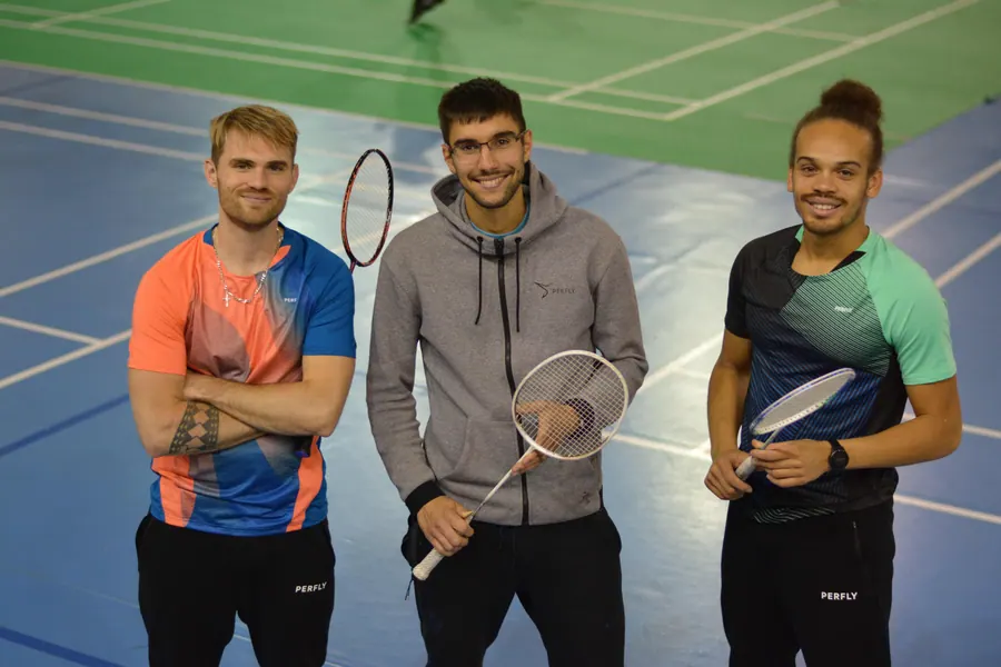 Trois coachs Fuzions, raquette en main, souriants, côte à côte sur un terrain de badminton