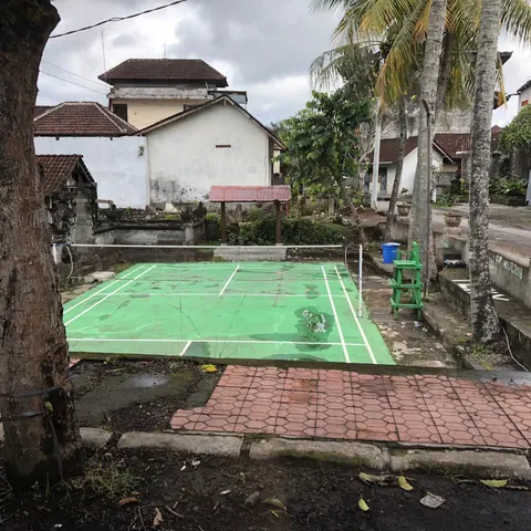 Un terrain de badminton extérieur, vert, entre les maisons d’un quartier de Bali