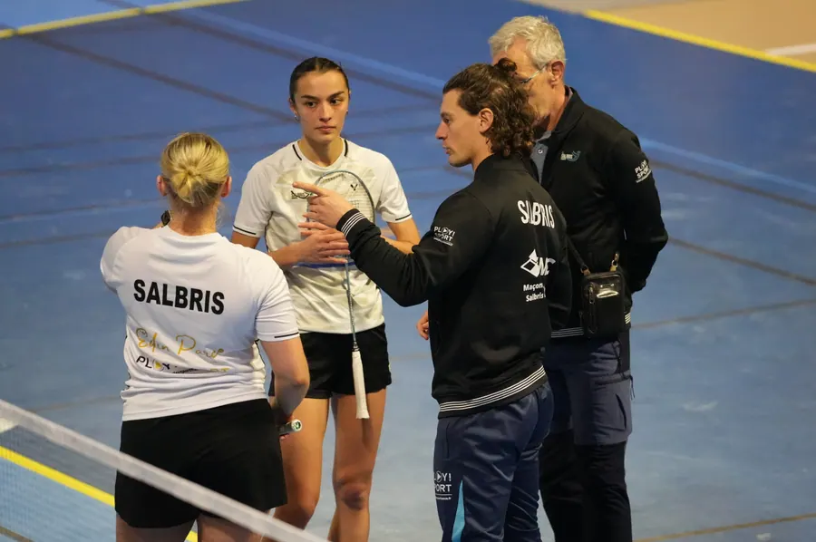 Maxime Michel, de profil, donne une consigne à deux joueuses au bord du terrain pendant un match, un autre coach à ses côtés
